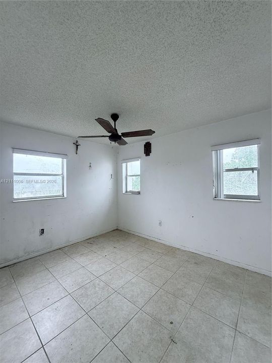 Interior room featuring ceramic tile flooring, three windows with roller shades, and a ceiling fan