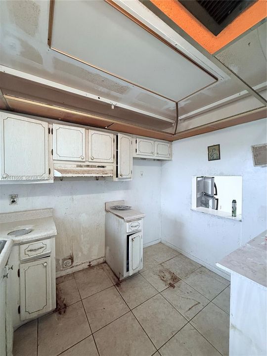 Kitchen featuring white cabinetry, solid-surface countertops, tile flooring, and a recessed ceiling architectural detail