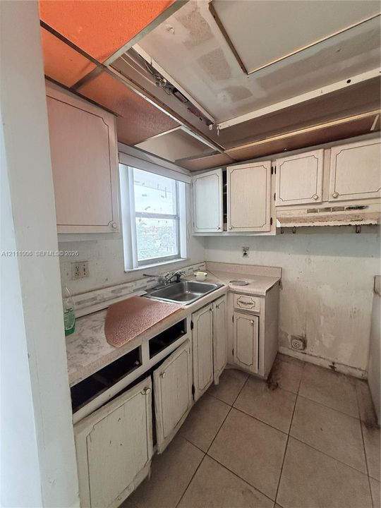 Kitchen featuring light-toned cabinetry, a stainless steel sink, tiled flooring, and a window providing natural lighting
