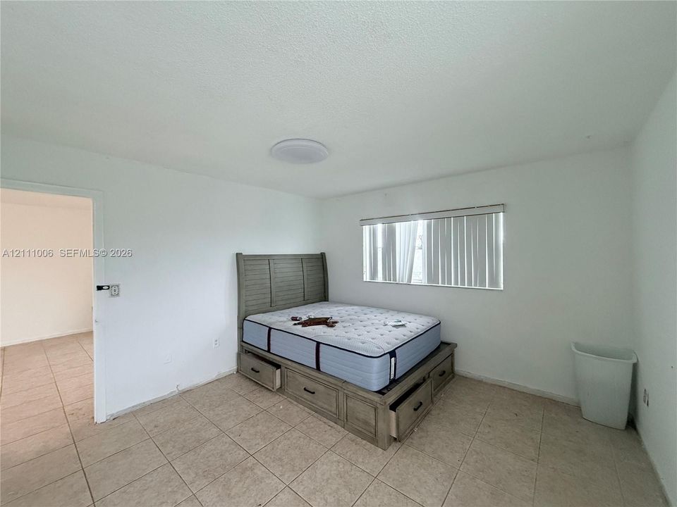 Neutral-toned tile flooring, flush-mount ceiling lighting, and vertical window blinds