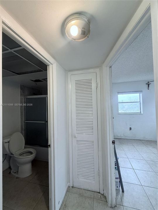 Full-height louvered closet door featuring a crisp white finish and a circular ceiling-mounted light fixture