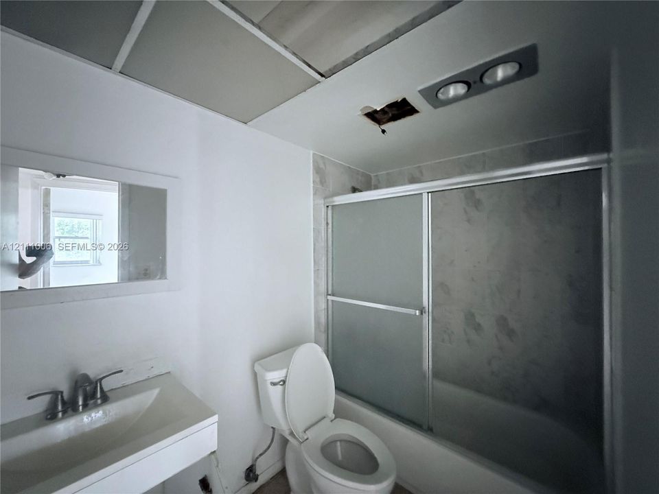 Wall-mounted mirror, white vanity with integrated sink, dual-handle faucet, and tub-shower combination with sliding glass doors
