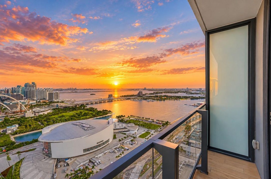Private balcony featuring wood-finish flooring, a glass panel railing, and expansive water and urban skyline scenery