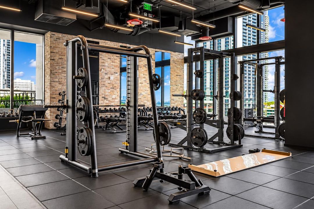 Fitness center featuring floor-to-ceiling windows, exposed brick accent walls, industrial-style exposed ceiling, and rubberized athletic flooring