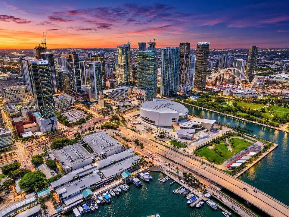 Aerial perspective of metropolitan skyline featuring high-rise architecture, proximity to waterfront, urban park spaces, and paved thoroughfares