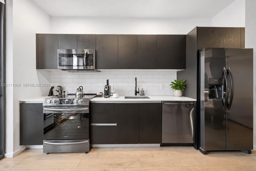 Kitchen featuring flat-panel cabinetry, quartz countertops, white subway tile backsplash, stainless steel appliances, and wood-finish flooring