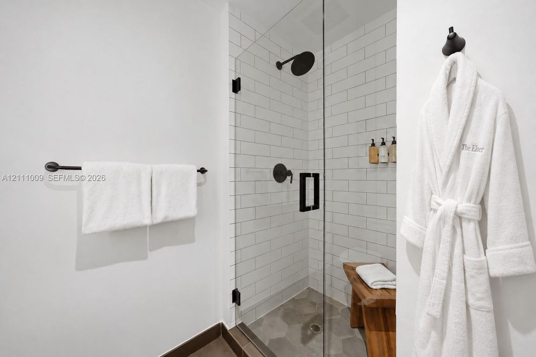 Walk-in shower featuring white subway tile surround, frameless glass door, matte black fixtures, and hexagonal floor tile