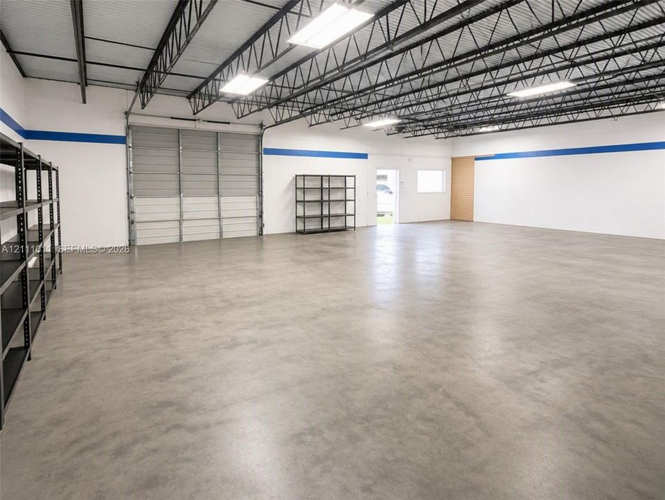 Expansive open-concept industrial space featuring polished concrete flooring, exposed steel truss ceiling, high-clearance roll-up door, and high-output overhead lighting