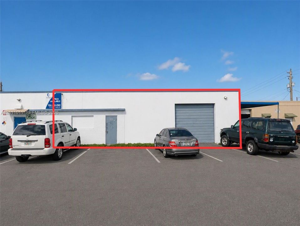 Commercial exterior featuring a white stucco facade, a metal roll-up bay door, and a dedicated entry door