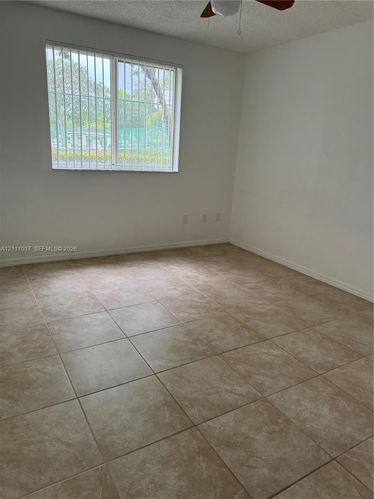 Neutral-toned ceramic tile flooring, multi-pane window with security bars, and a ceiling fan fixture