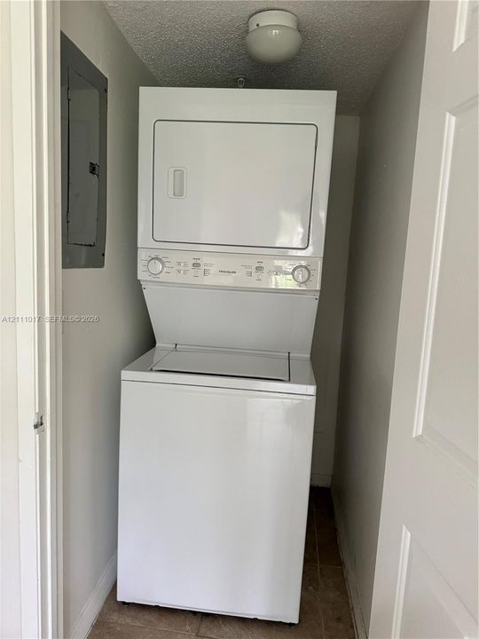 Stacked laundry unit featuring a top-load washer, a front-load dryer, and a recessed electrical service panel