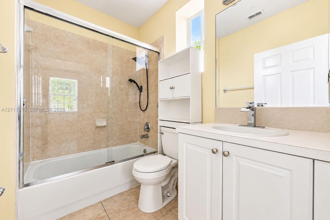 Bathroom featuring a shower-tub combination with a glass sliding enclosure, tile-surround walls, vanity with a solid-surface countertop, and a built-in storage cabinet