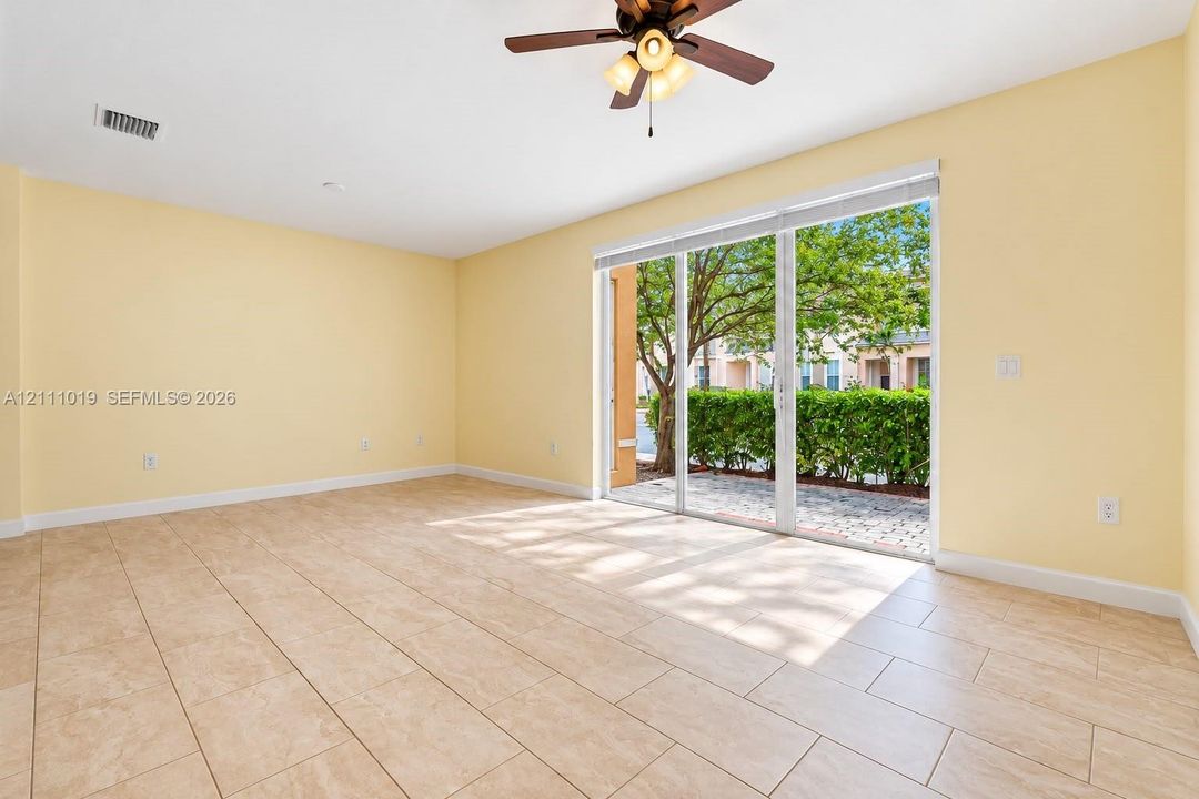Interior space featuring large-format ceramic tile flooring, neutral wall paint, three-panel sliding glass doors, and a ceiling fan with integrated light fixture
