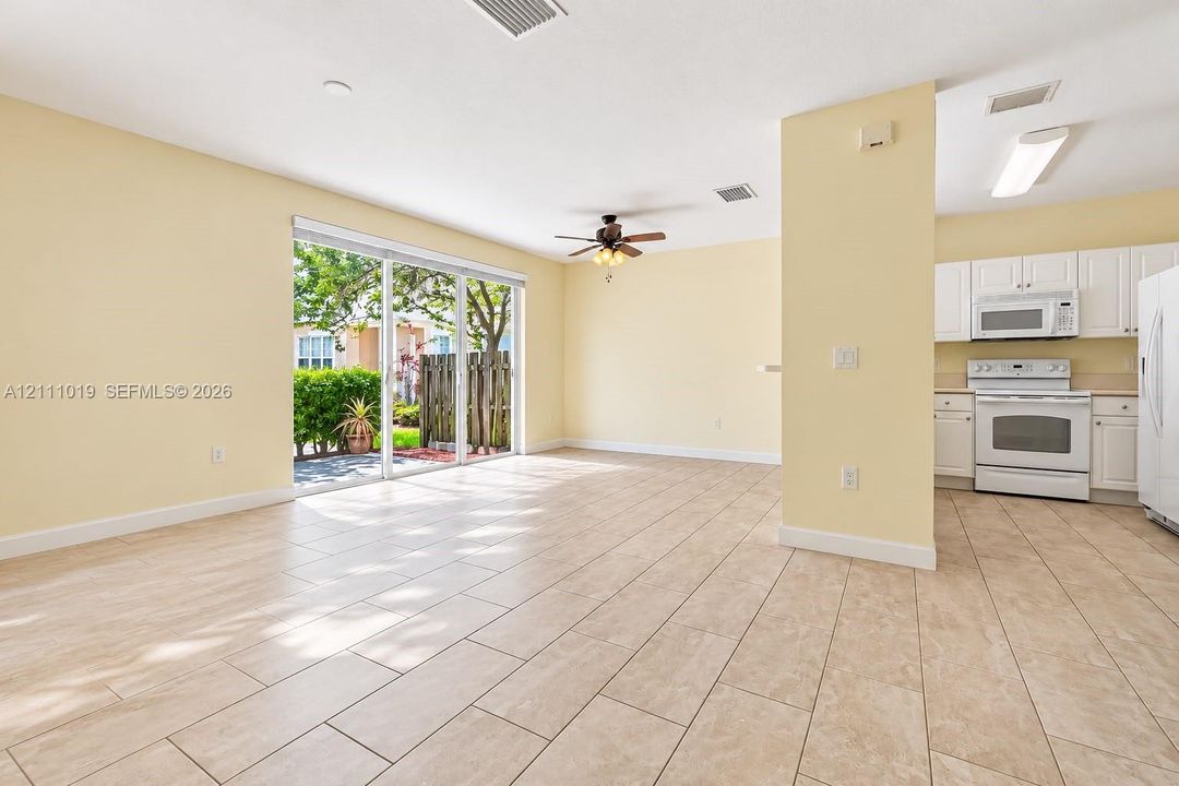 Open-concept area featuring light-toned tile flooring, white cabinetry, integrated white appliances, and sliding glass doors with exterior access