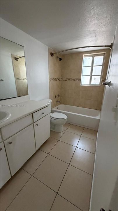 Bathroom featuring ceramic tile flooring, a porcelain tub with tile surround, a single-sink vanity, and a rectangular window