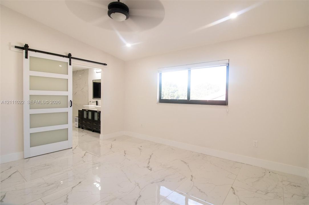 Polished tile flooring with veining, white barn-style sliding door with frosted glass panels, black hardware, recessed ceiling lighting, and a black-frame window
