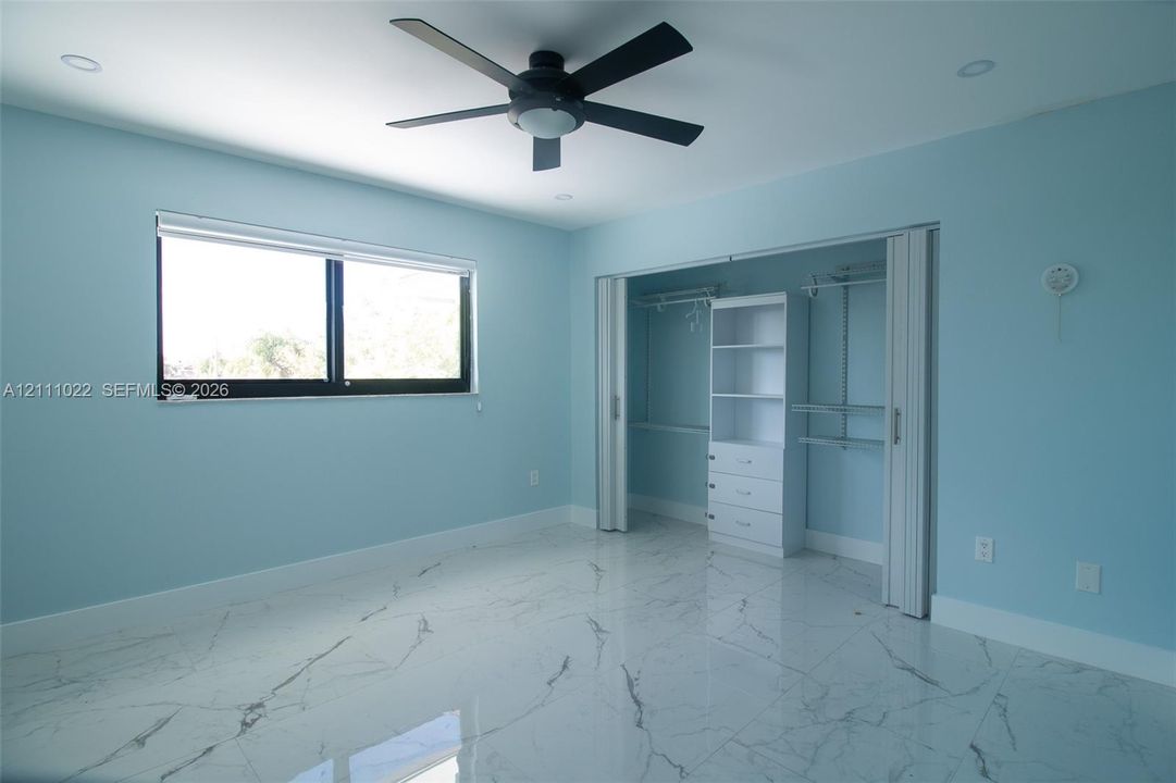 Polished stone-look tile flooring, recessed lighting, matte black ceiling fan, dual-pane window with black framing, and reach-in closet featuring integrated shelving and drawer storage