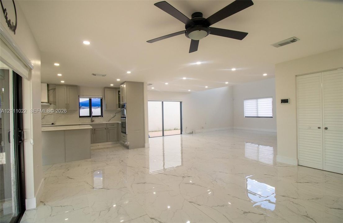 Open-concept space featuring polished stone-finish flooring, recessed lighting, a modern kitchen with quartz countertops, custom cabinetry, and a ceiling fan