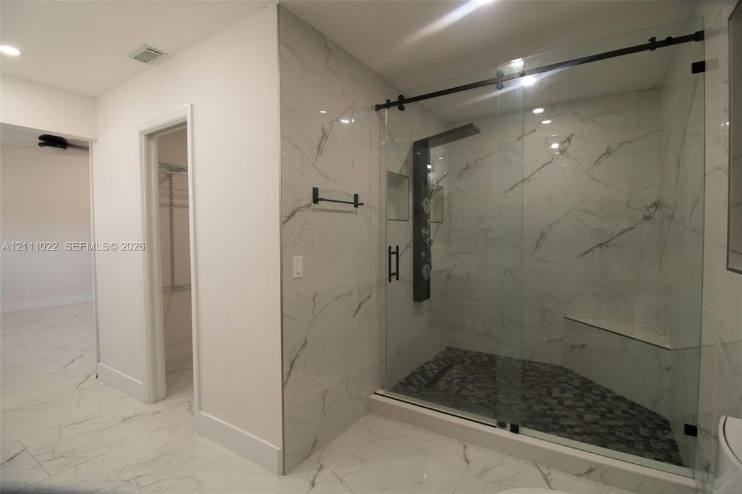 Walk-in shower with floor-to-ceiling stone-finish tile, glass sliding door, built-in bench, and multi-head shower system