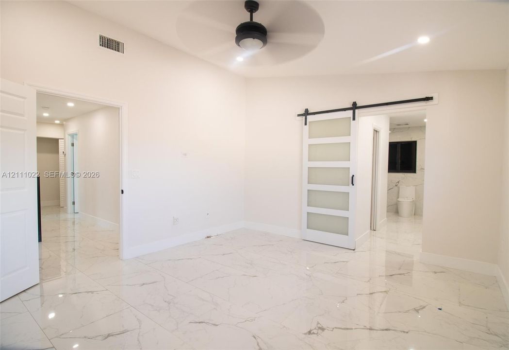 Interior space featuring large-format tile flooring with a marble-style finish, vaulted ceilings with a matte black ceiling fan, and a white sliding barn door with frosted glass panels