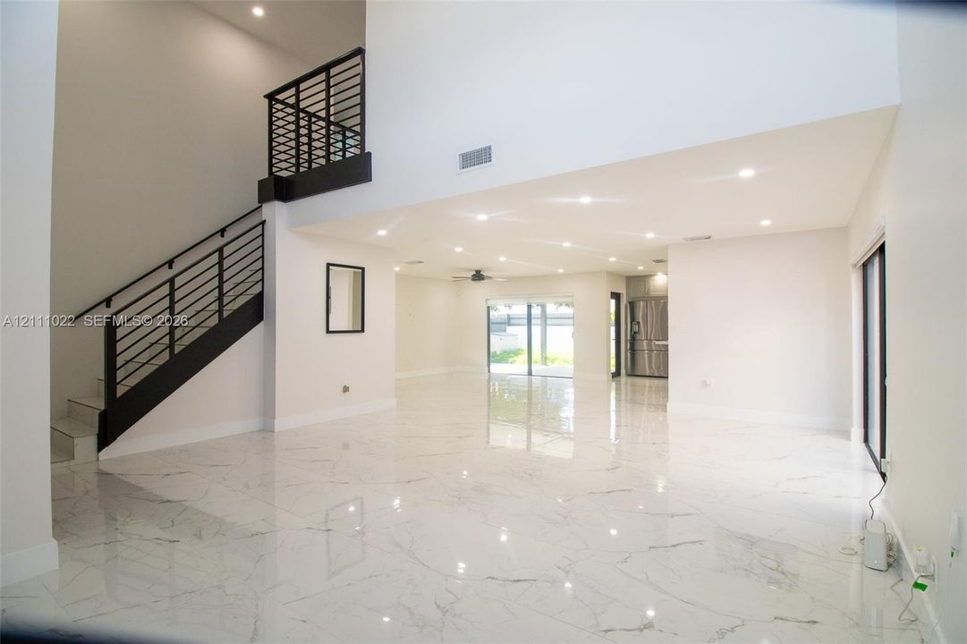 Double-height ceiling, polished stone-finish flooring, staircase with horizontal metal railing, and recessed ceiling lighting