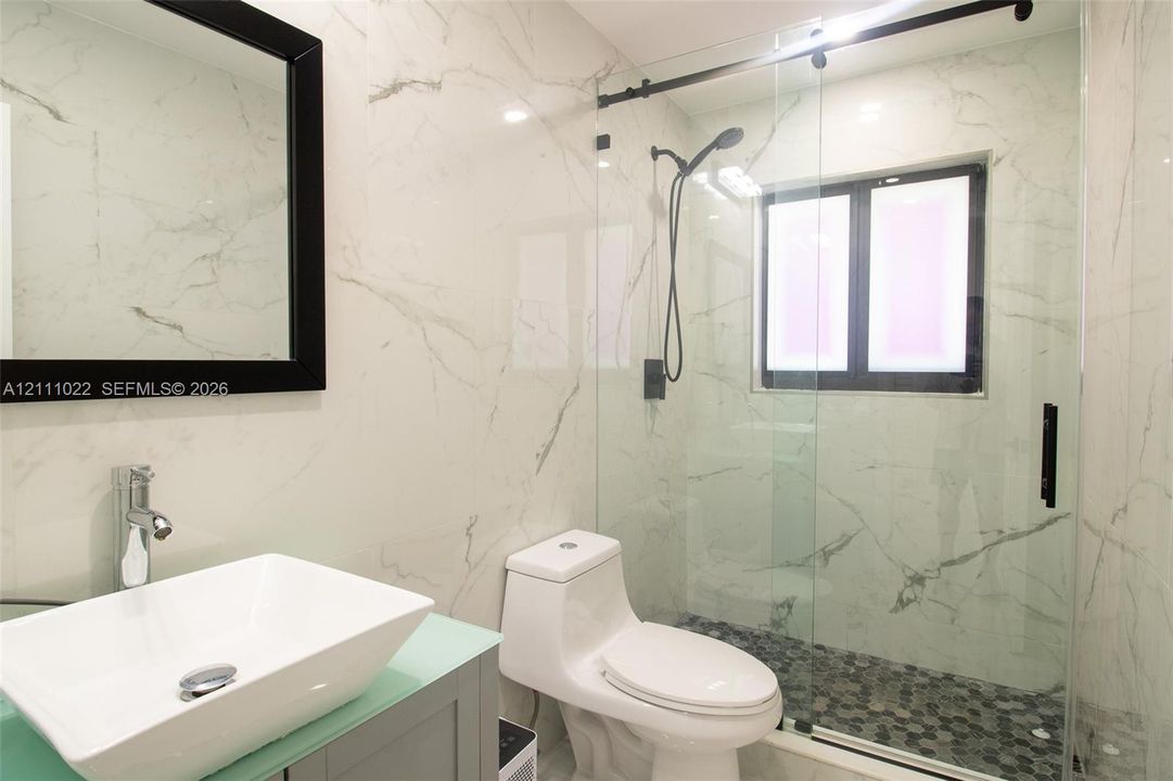 Bathroom featuring floor-to-ceiling veined tile, a vessel sink with a chrome faucet, a frameless glass shower enclosure with matte black hardware, and hexagonal mosaic shower floor tiling