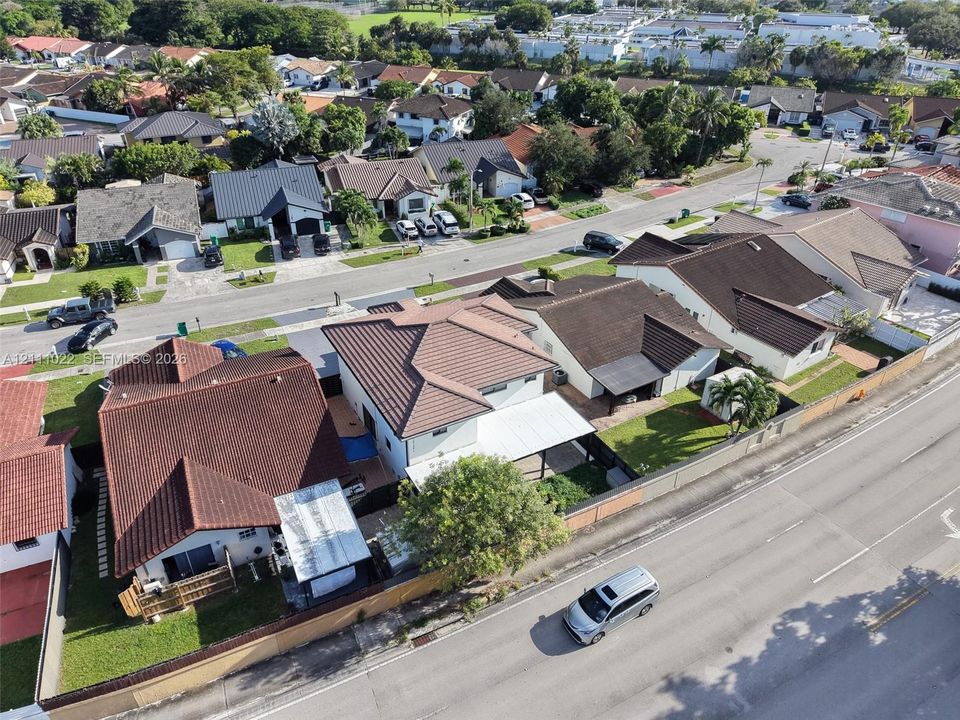 Aerial perspective showcasing a residential property with a multi-hipped roofline, integrated covered rear patio, and fenced perimeter