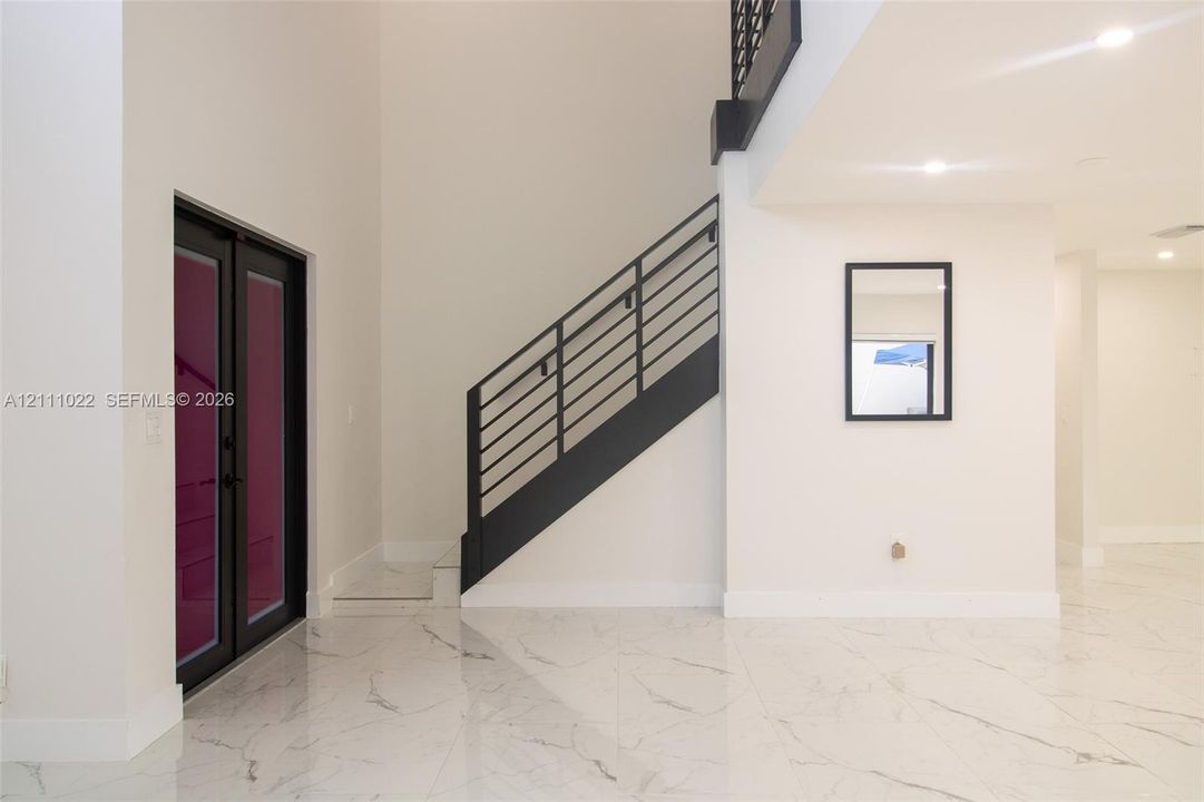 High-ceiling entryway featuring large-format stone-finish tile flooring, a dual-entry door with black frame, and a staircase with a black metal railing