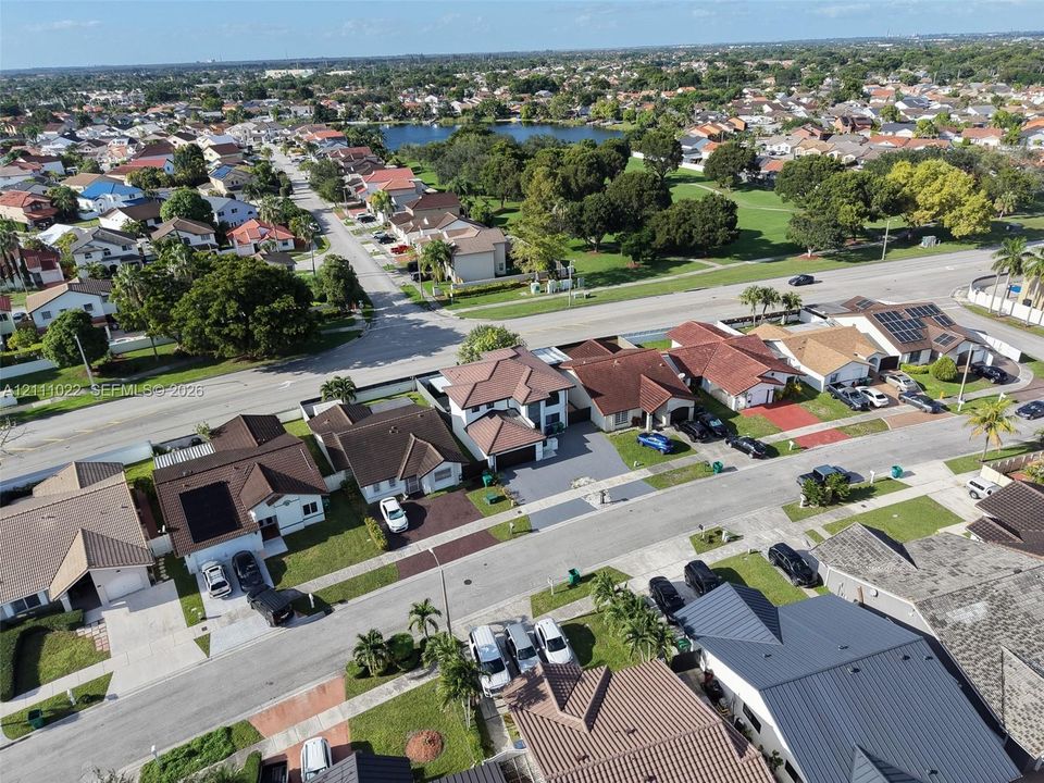 Aerial perspective of a residential neighborhood featuring paved streets, mature trees, multi-roofline homes, and surrounding green spaces