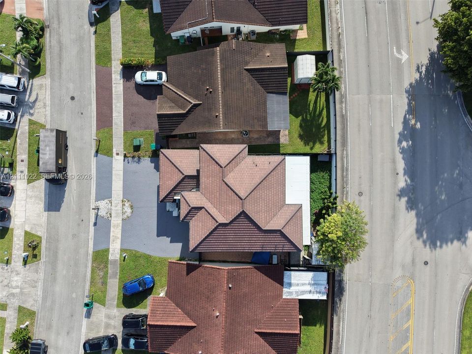 Aerial perspective of a multi-gabled residence featuring a concrete tile roof, paved driveway, and dedicated rear patio space