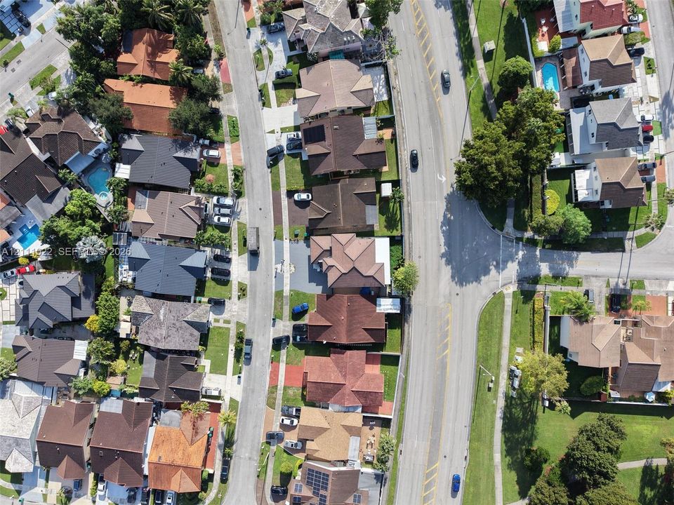 Aerial perspective of a suburban neighborhood featuring residential dwellings, mature tree canopy, varied shingle rooflines, and paved street infrastructure