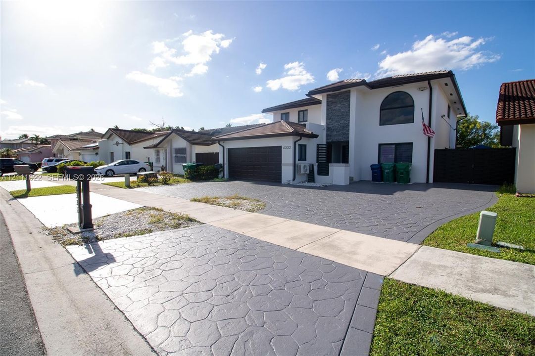 Two-story stucco exterior featuring a stone-veneer accent wall, multi-textured paved driveway, attached two-car garage, and arched architectural window