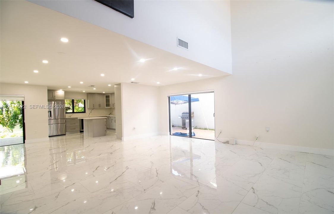 Open-concept interior featuring high ceilings, large-format tile flooring with a stone-inspired pattern, recessed lighting, and sliding glass doors
