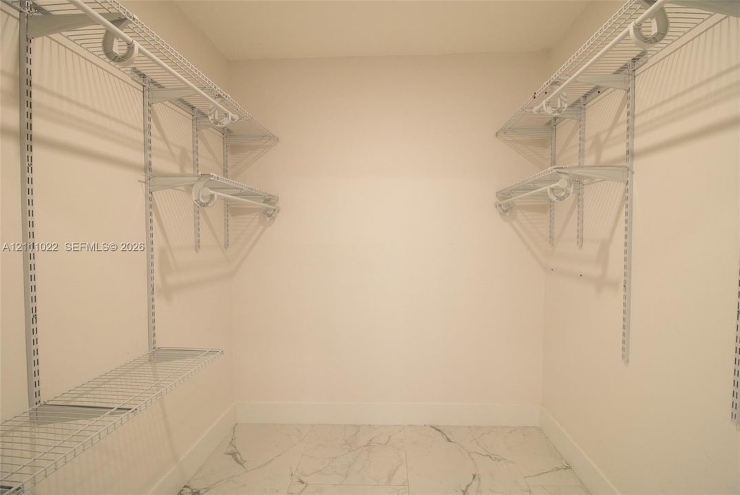 Storage area featuring adjustable metal wire shelving, wall-mounted supports, and stone-finish flooring