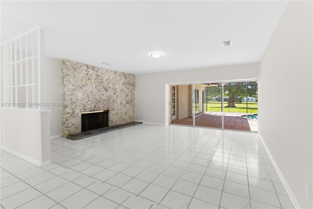 Living area featuring tile flooring, a floor-to-ceiling stone fireplace, a partial-height decorative room divider, and sliding glass doors opening to a screened lanai
