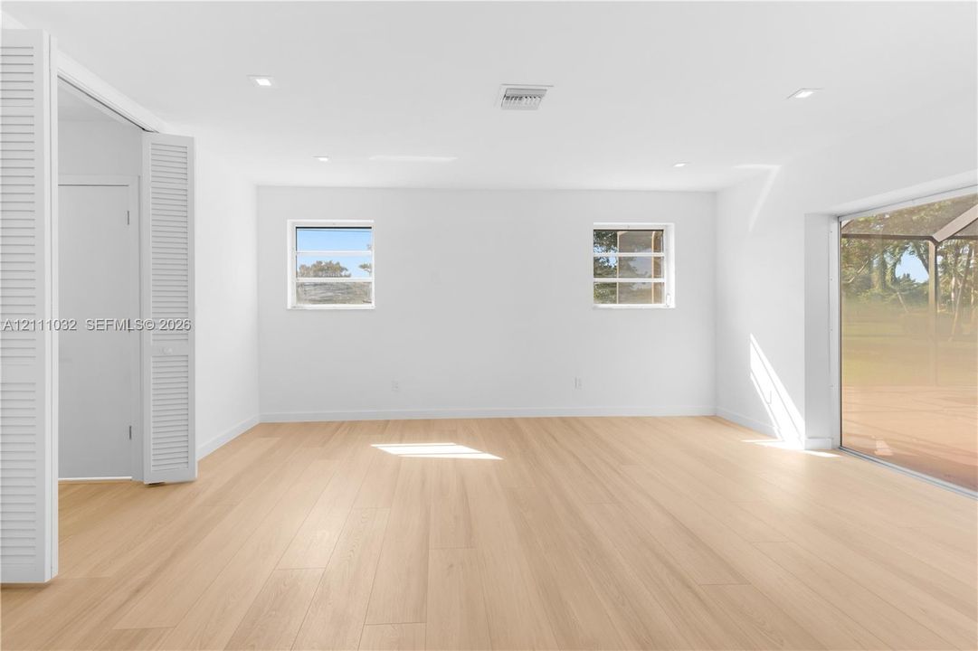 Light-filled interior featuring wood-finish flooring, recessed lighting, white louvered closet doors, and large sliding glass panels