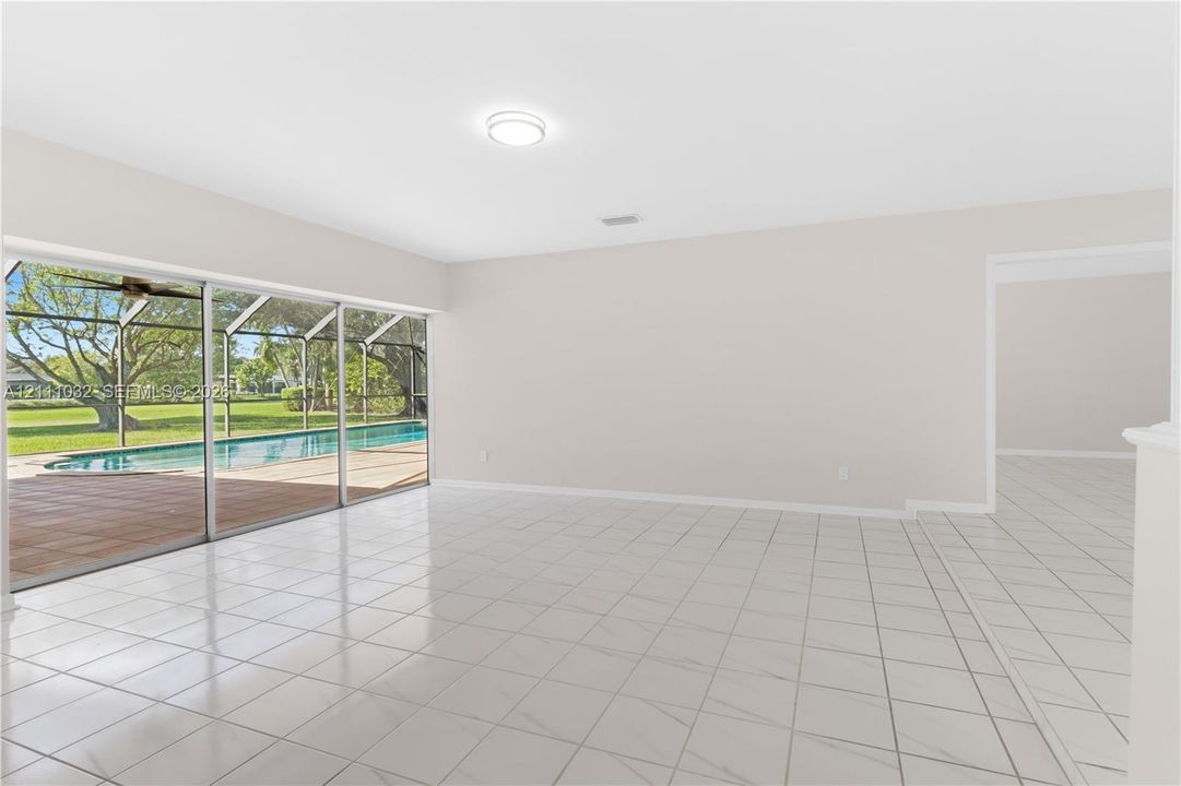 Open-concept interior featuring oversized tile flooring, recessed ceiling lighting, and expansive floor-to-ceiling sliding glass doors leading to a screened-in patio and swimming pool