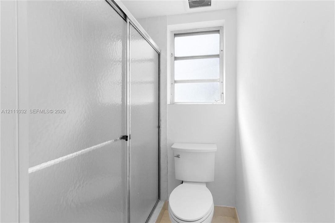 Shower enclosure with textured glass sliding doors, white ceramic toilet, and a window with frosted glass