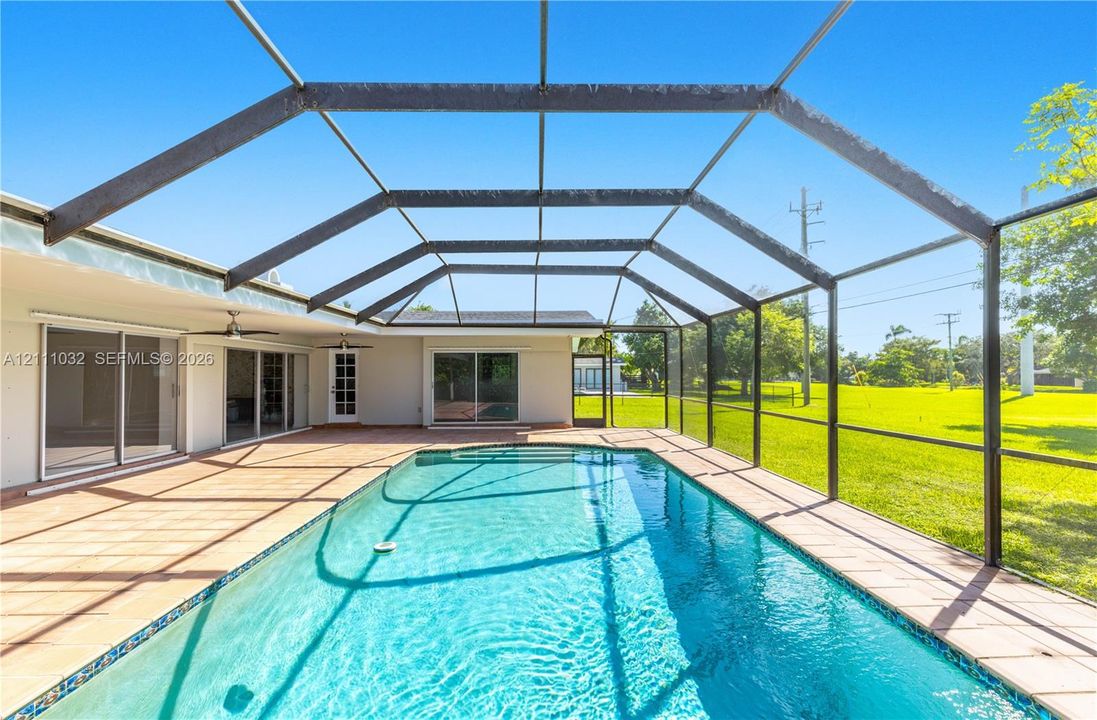 Screen-enclosed pool deck featuring tile flooring, a rectangular swimming pool, and multiple sliding glass door access points