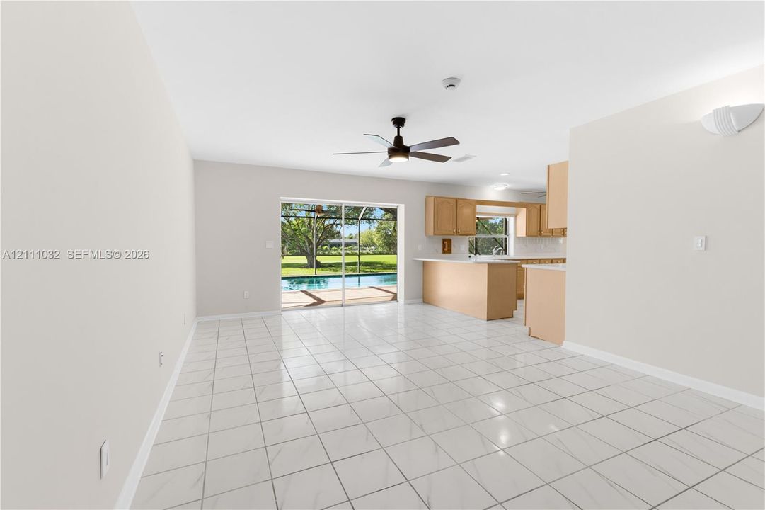 Open-concept interior featuring light-toned cabinetry, a kitchen island, neutral tile flooring, a ceiling fan, and sliding glass doors leading to a screened lanai with a pool