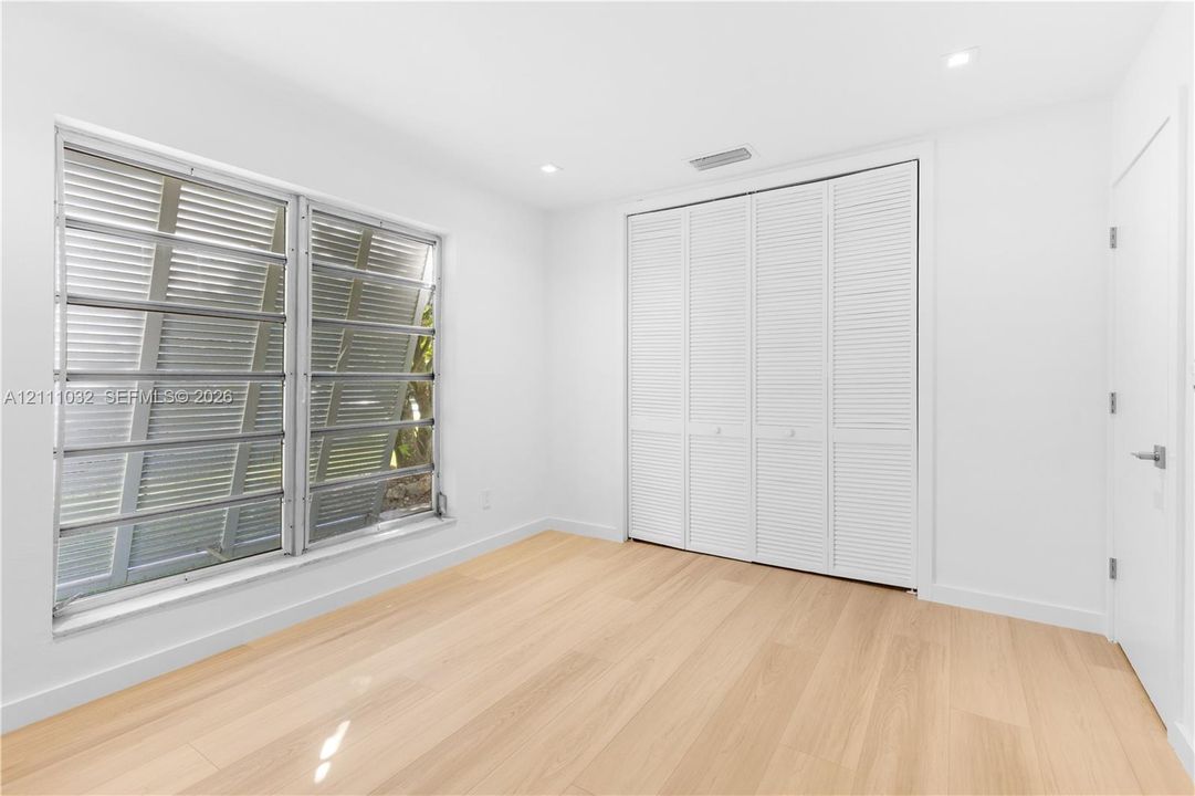 Room featuring wood-finish flooring, recessed lighting, white louvered closet doors, and multi-pane jalousie windows