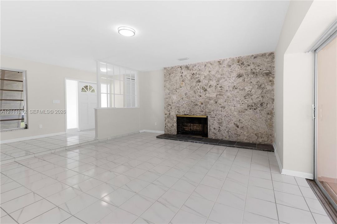 Floor-to-ceiling stone fireplace surround, tile flooring, glass-paneled room divider, sliding glass door, and flush-mount lighting