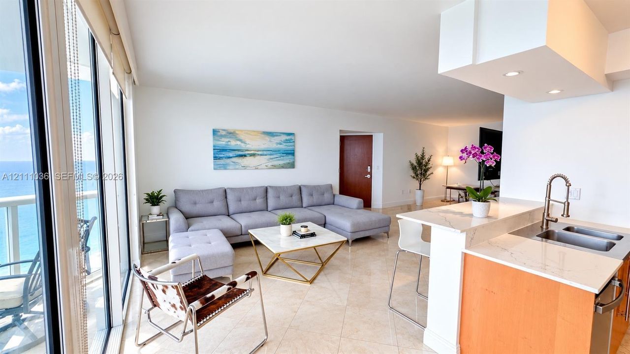 Open-concept living space featuring floor-to-ceiling windows, natural stone flooring, kitchen peninsula with a quartz countertop, and recessed lighting