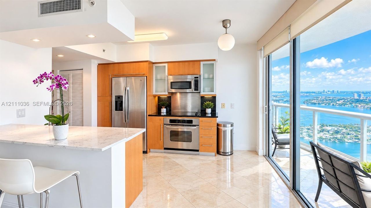 Kitchen featuring wood-finish cabinetry, stainless steel appliances, stone-topped island, polished tile flooring, and floor-to-ceiling glass sliding doors