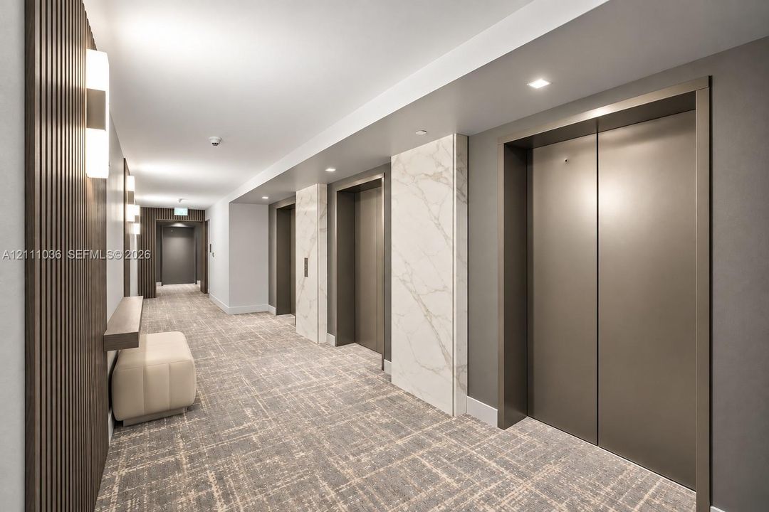Elevator lobby featuring metallic-finish elevator doors, floor-to-ceiling stone-clad surround, wood-slat accent wall, and recessed lighting