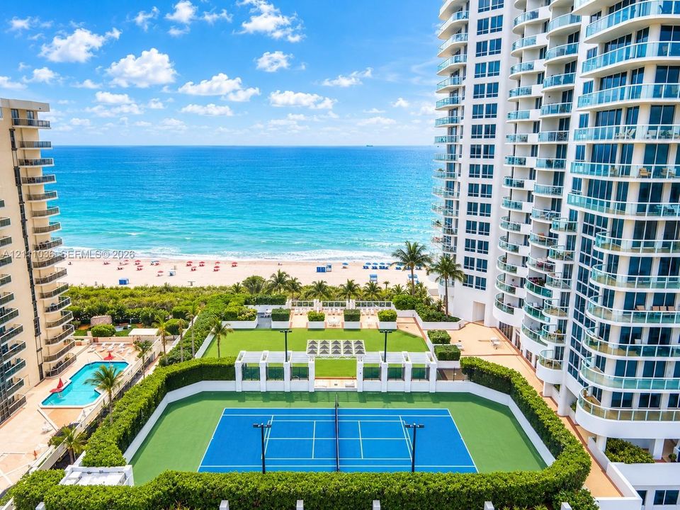 High-rise property featuring a private tennis court, outdoor swimming pool, manicured lawn area, and tiered balconies