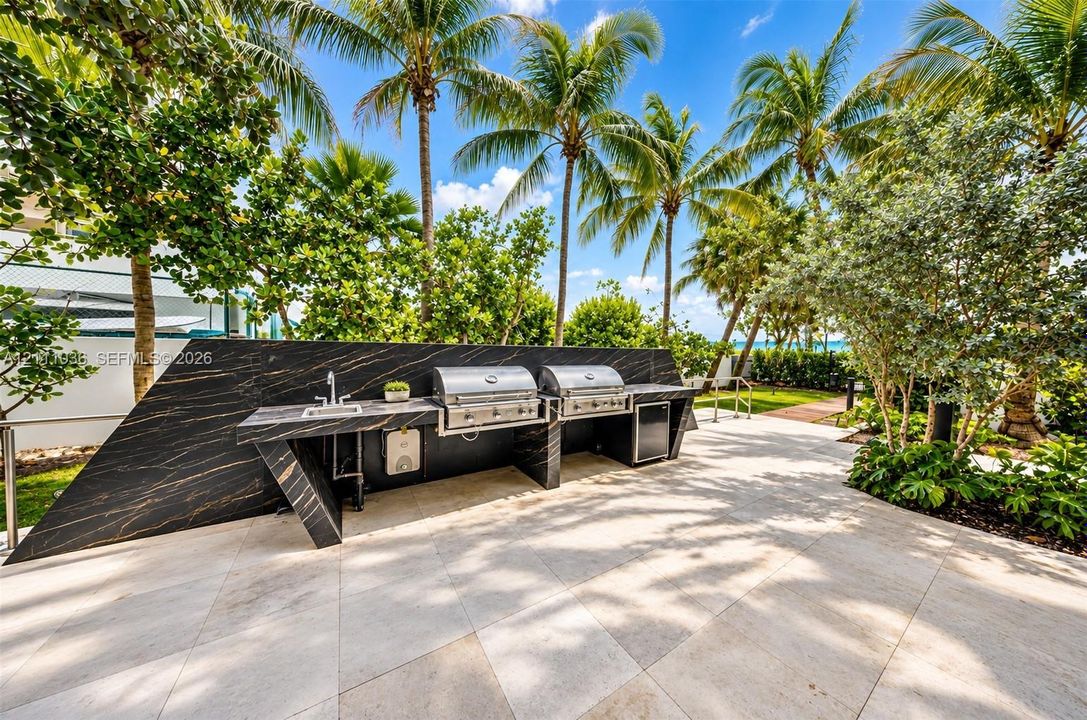 Outdoor kitchen featuring a sleek, dark-veined stone countertop, built-in stainless steel dual grills, an integrated stainless steel sink, and light-toned tile flooring