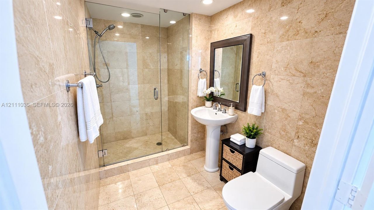 Full-height natural stone wall tiling, walk-in glass-enclosed shower, pedestal sink, and polished chrome fixtures