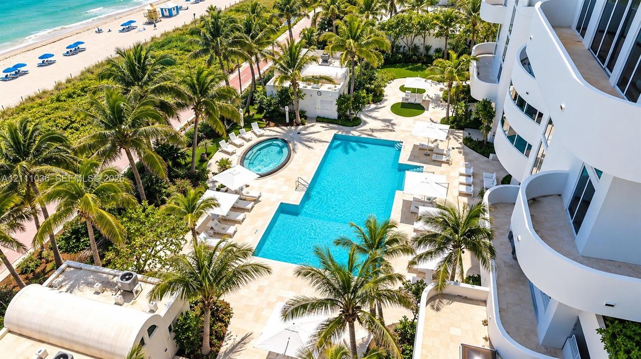 Oceanfront swimming pool and spa surrounded by stone decking, mature palm trees, and multi-level curved balconies