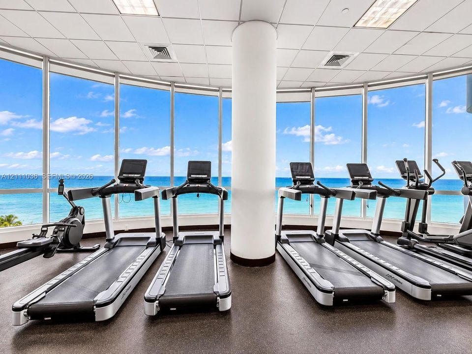 Fitness center featuring floor-to-ceiling panoramic windows, ocean horizon exposure, and a central structural column